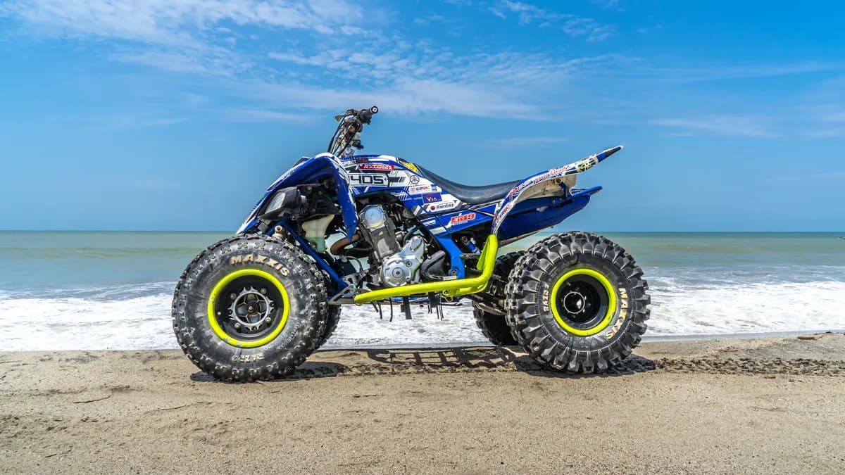 A detailed image of a quad bike parked on a sandy beach under a clear blue sky.
