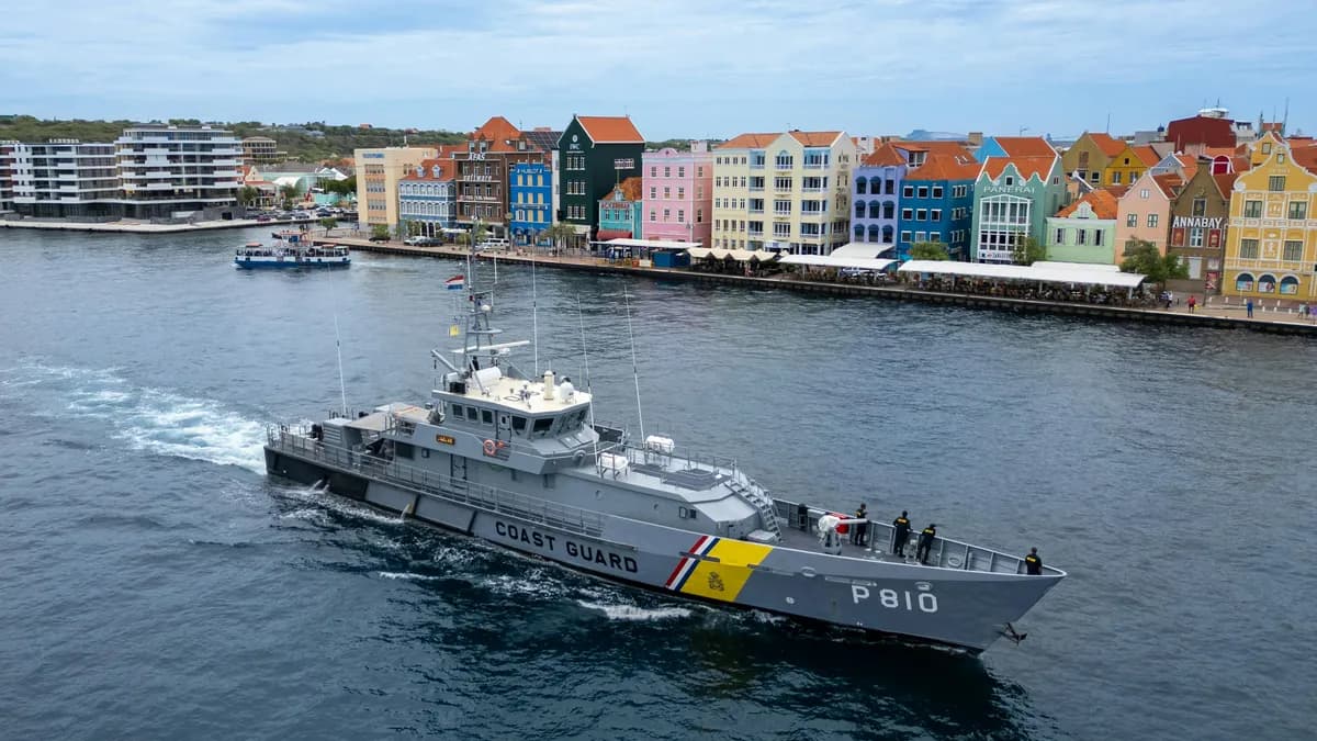 A Coast Guard vessel cruises through the waters of Willemstad, Curaçao, with the city’s iconic colorful Dutch colonial buildings in the background.